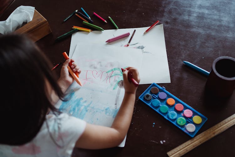 Girl Drawing On Paper With Crayons