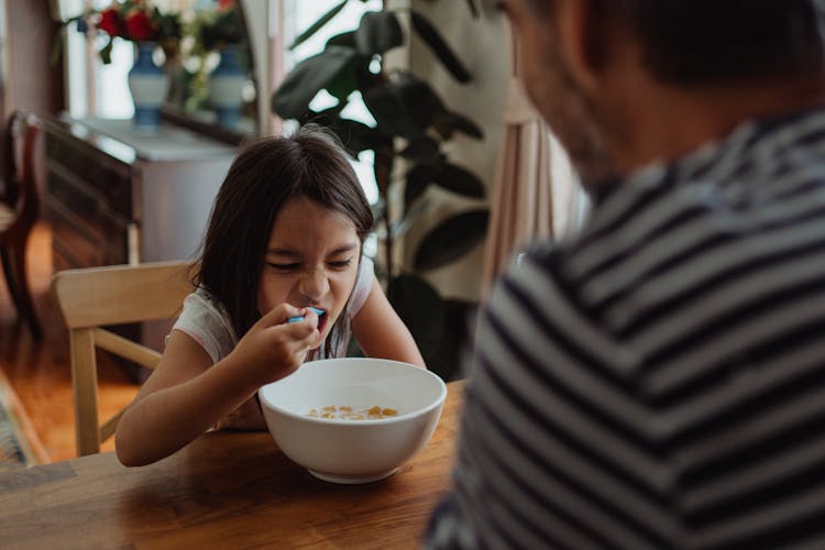 A Girl Pulling A Funny Face While Eating A Bowl Of Cereal