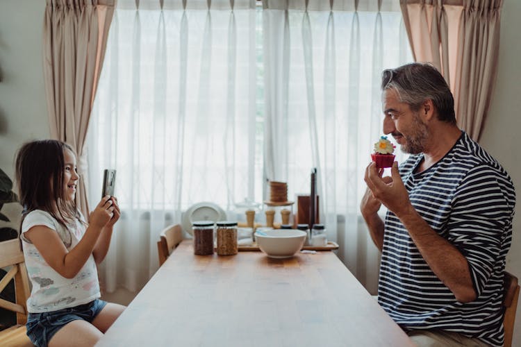 Little Girl Making Photo Of Father And Cupcake