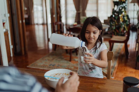 A girl pours milk into a glass, preparing breakfast in a cozy home setting.