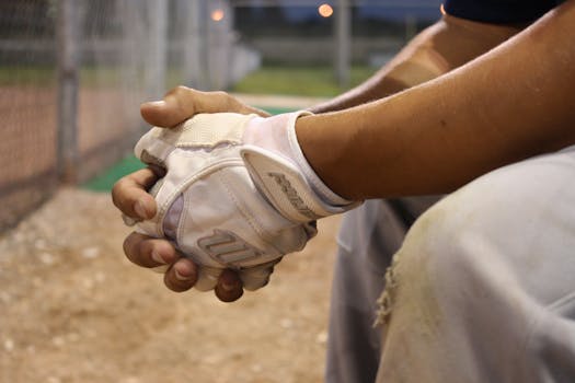 Close-up of a baseball player's hands with gloves during a game at dusk.