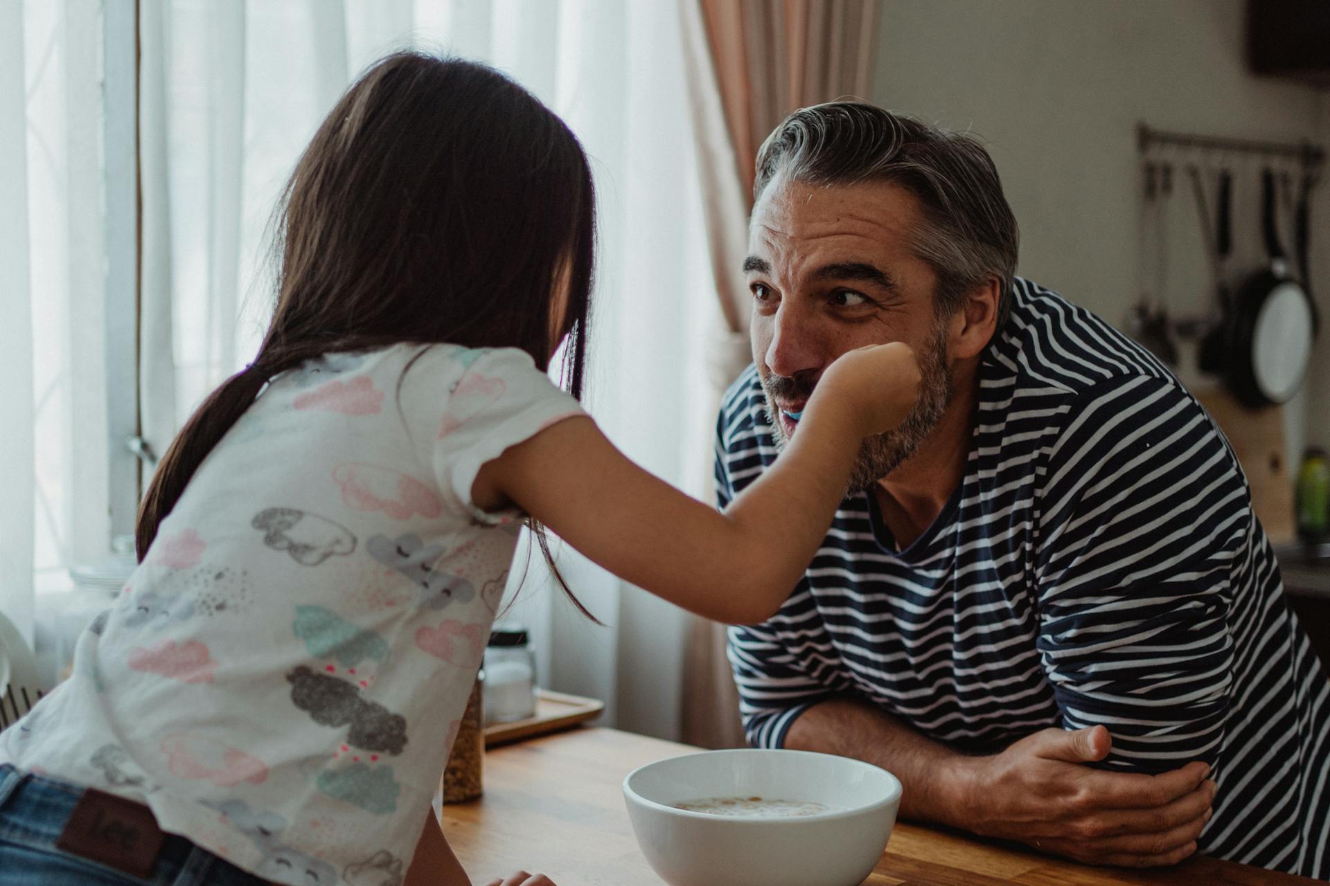 Daughter Feeding Her Father Cereal For Breakfast