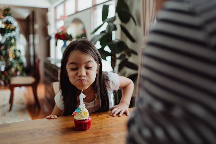 Girl Blowing Out A Candle On A Cupcake At Christmas