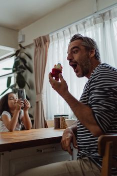 父亲拿着纸杯蛋糕开玩笑，女儿在室内拍照