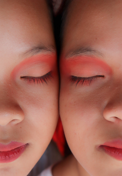 Artistic twin portrait with vibrant red eye shadow and closed eyes.