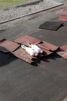 一对双胞胎身着白色连衣裙，躺在户外阳光下的垫子上，画面宁静而对称