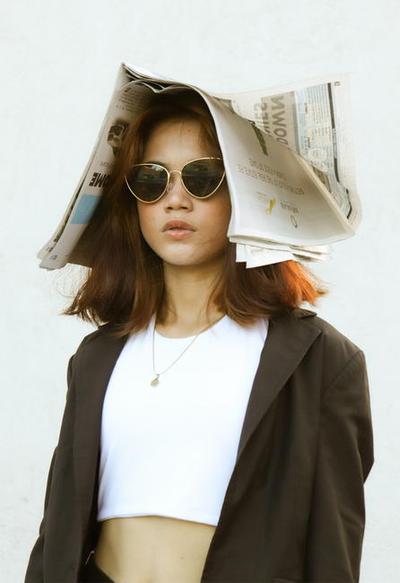 Stylish woman in sunglasses and suit coat with a creative newspaper hat on a white background.