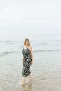 一名赤脚女子穿着连衣裙、留着短发，沿着平静的海滩散步