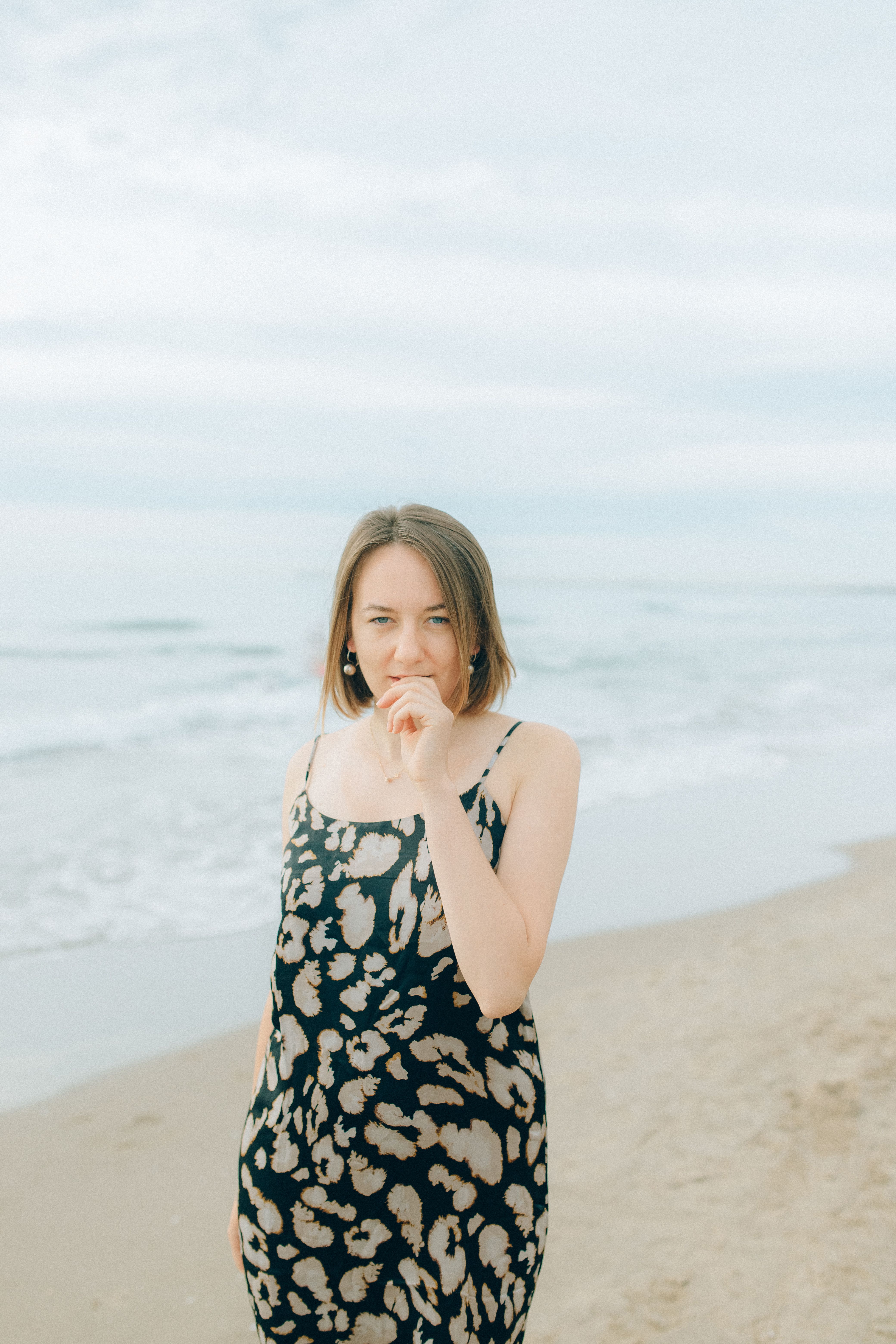 一名短发女子穿着图案连衣裙，站在海边沙滩上