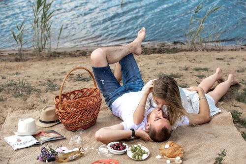 Free Couple enjoying a romantic picnic by a serene lakeside on a sunny day. Stock Photo