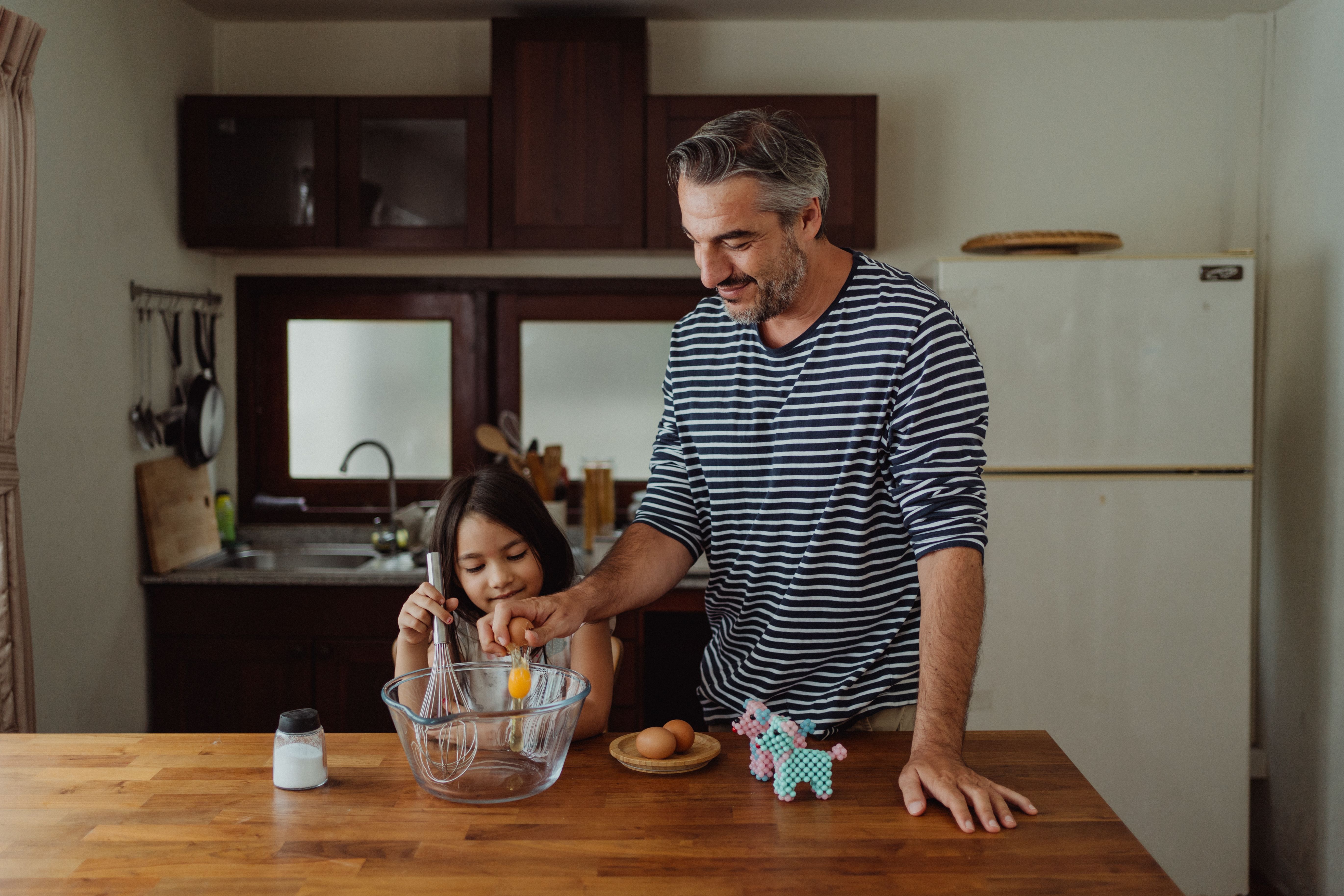 A father and daughter bonding while baking in a cozy kitchen setting.