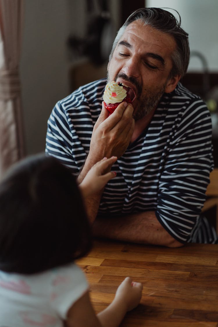 
A Bearded Man In A Striped Shirt Eating A Cupcake