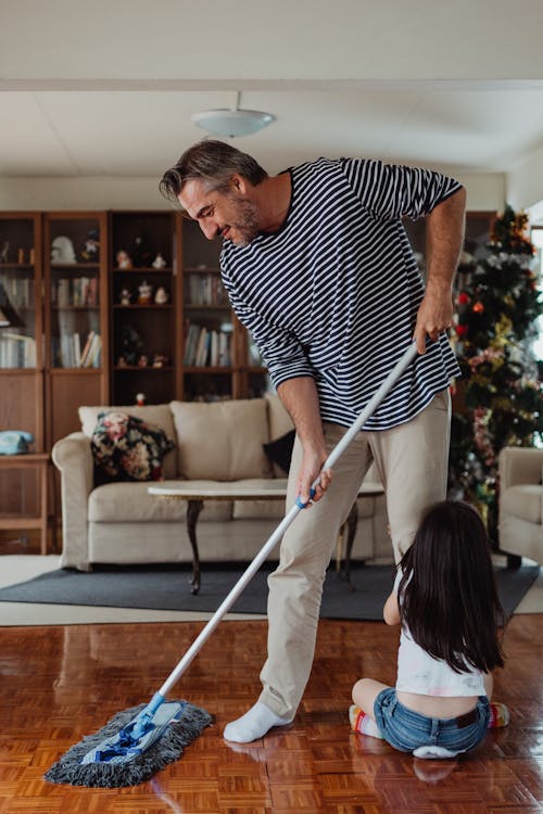 Free Father Cleaning House with his Daughter Holding his Leg Stock Photo