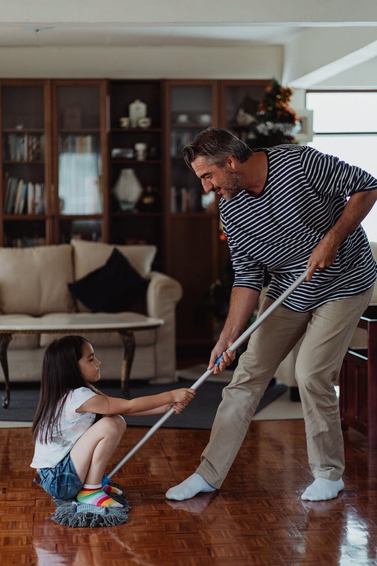 Father Mopping The Floor And Daughter Sitting on The Mop 