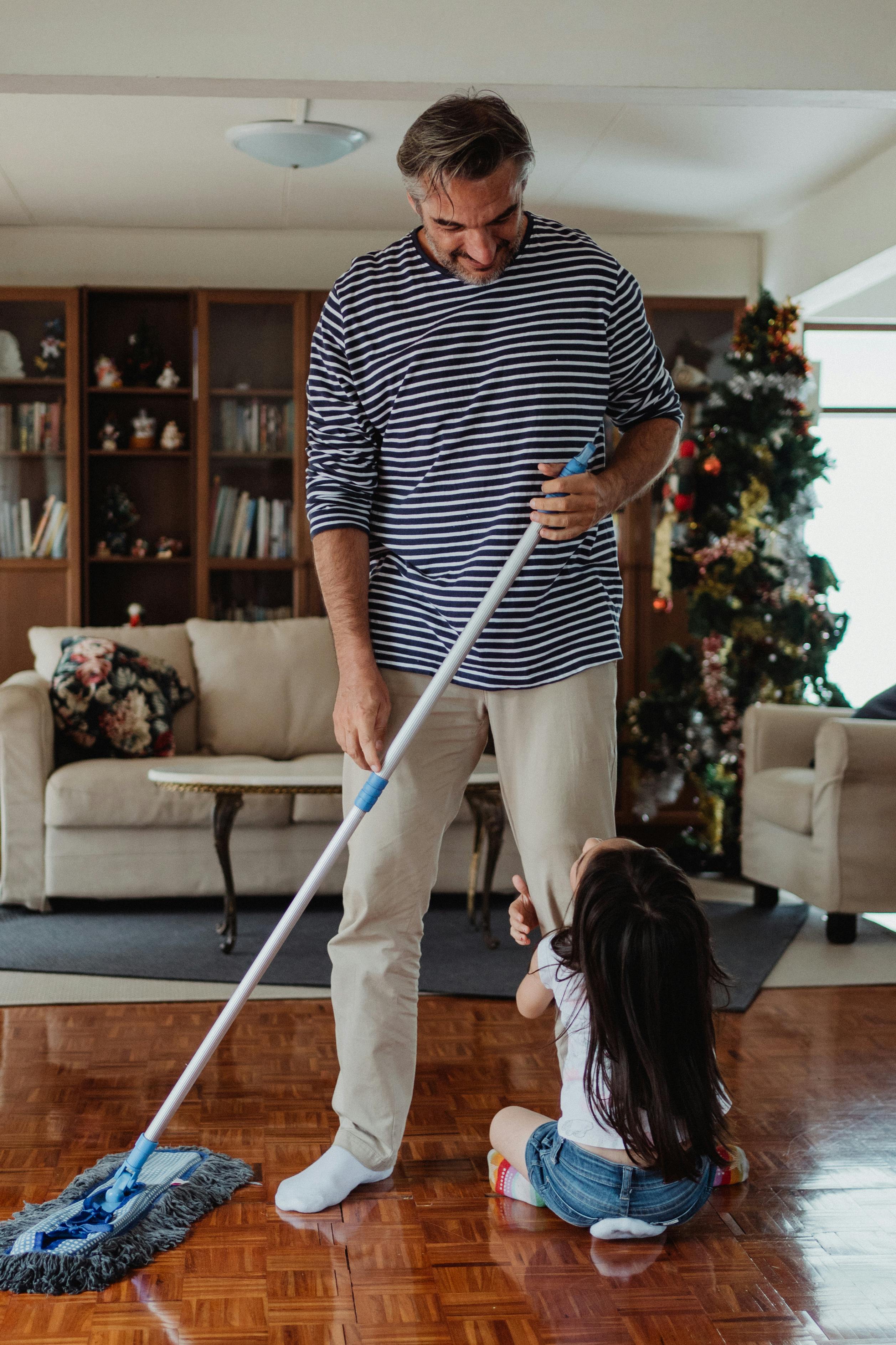 Father Mopping the Floor and Daughter Sticking to His Leg · Free Stock