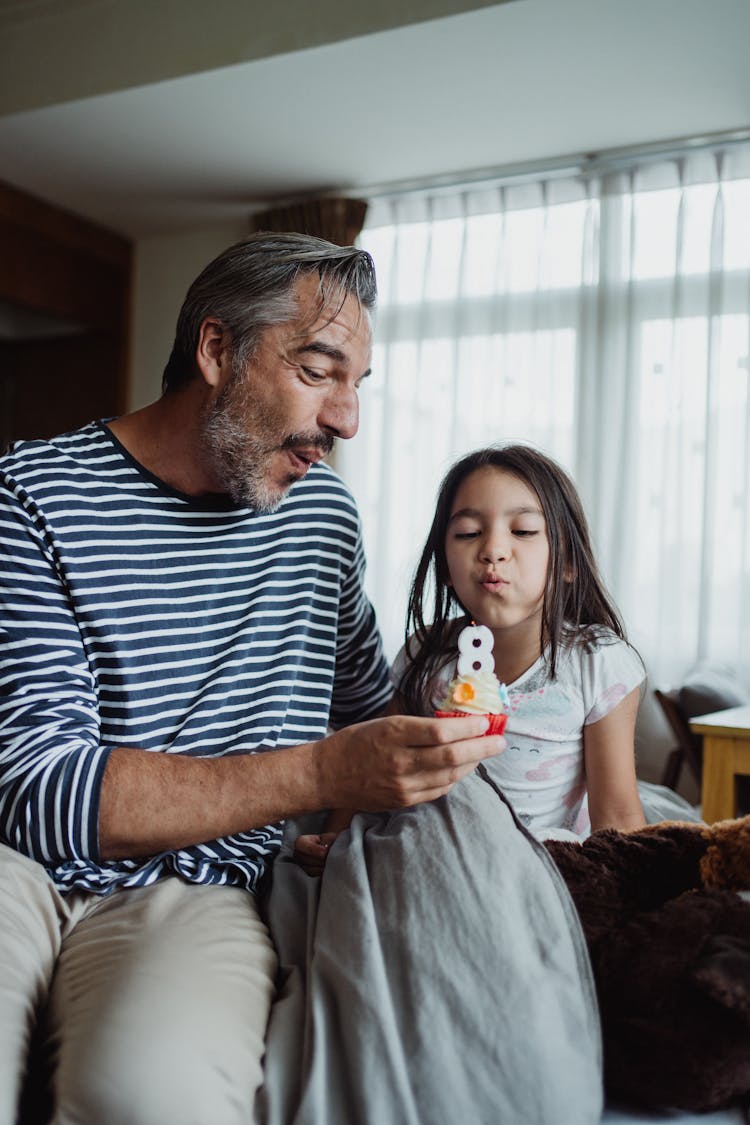 Father And Daughter Blowing Out A Candle On A Birthday Cupcake