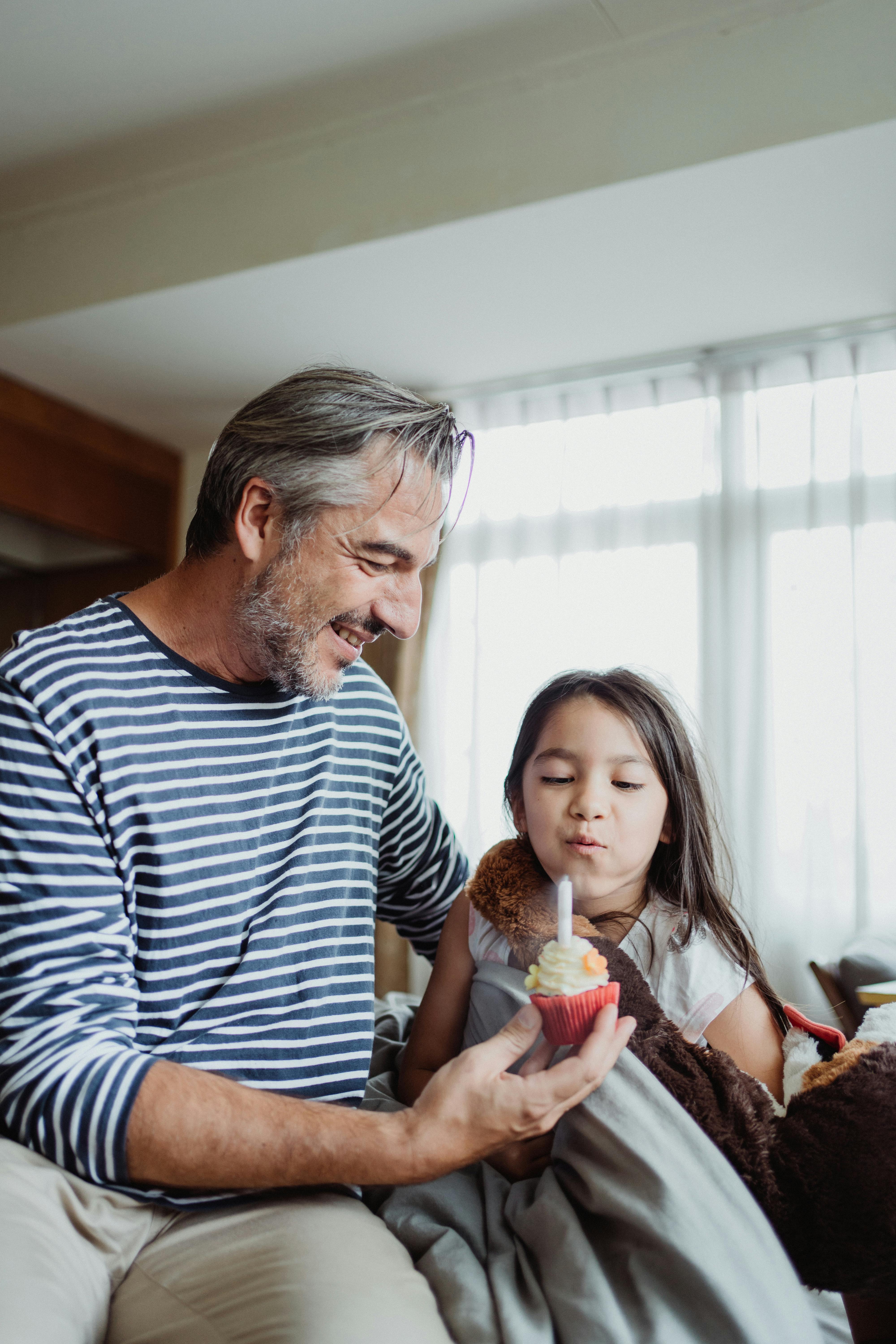 father with daughter blowing out a candle on a cupcake