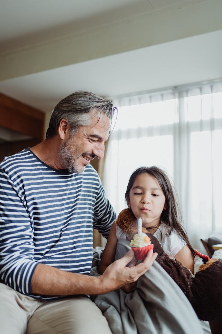 Father With Daughter Blowing Out A Candle On A Cupcake