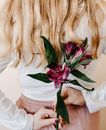 Unrecognizable female with long blond hair in casual clothes holding fresh flower behind back