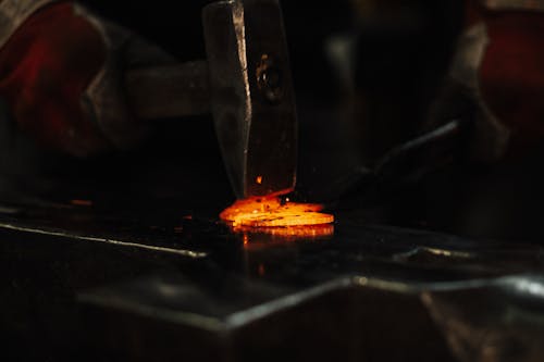Free High angle of crop anonymous male blacksmith using hammer while forging metal detail in workshop Stock Photo