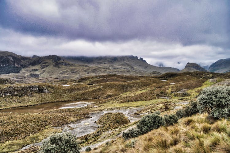 Green Grass Field And Mountain Under White Clouds