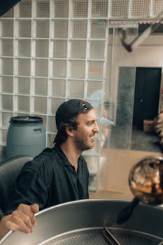 A man smiles while operating a modern coffee roasting machine in an industrial setting.