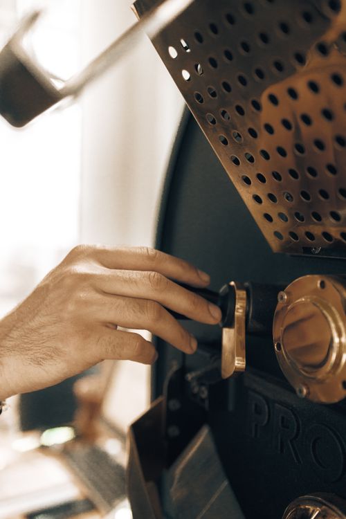 Free A hand adjusts controls on a modern coffee roaster inside a factory setting. Stock Photo
