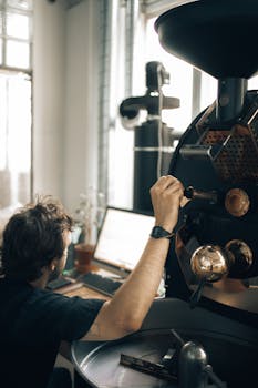 A man adjusting a modern coffee roaster in an industrial workshop, focusing on coffee production.