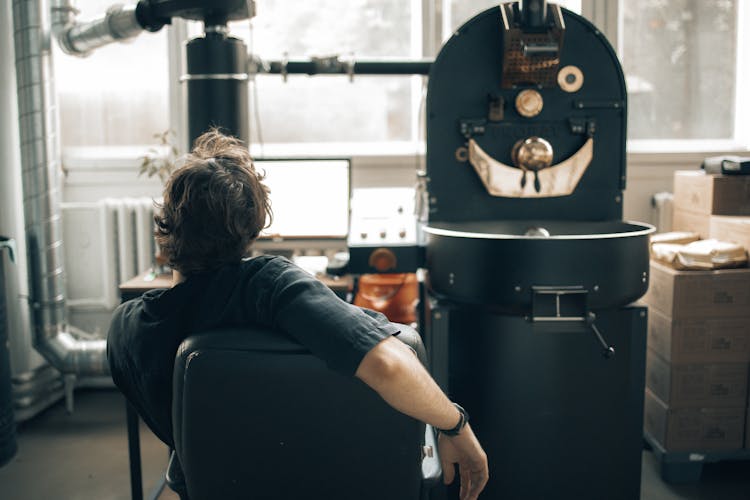 Man Operating A Machine At A Coffee Roasting Factory And Using A Computer 