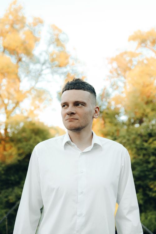 Free Portrait of a young man in a white shirt standing in a park with autumn foliage. Stock Photo