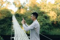 一名穿着条纹衬衫的男子在吊桥上用智能手机拍摄侧面风景