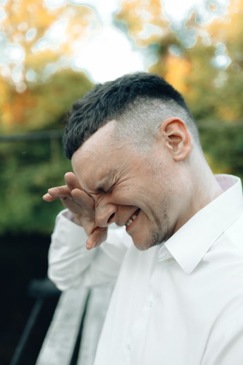 Free Man wearing a white shirt outdoors, expressing emotion amid greenery. Stock Photo