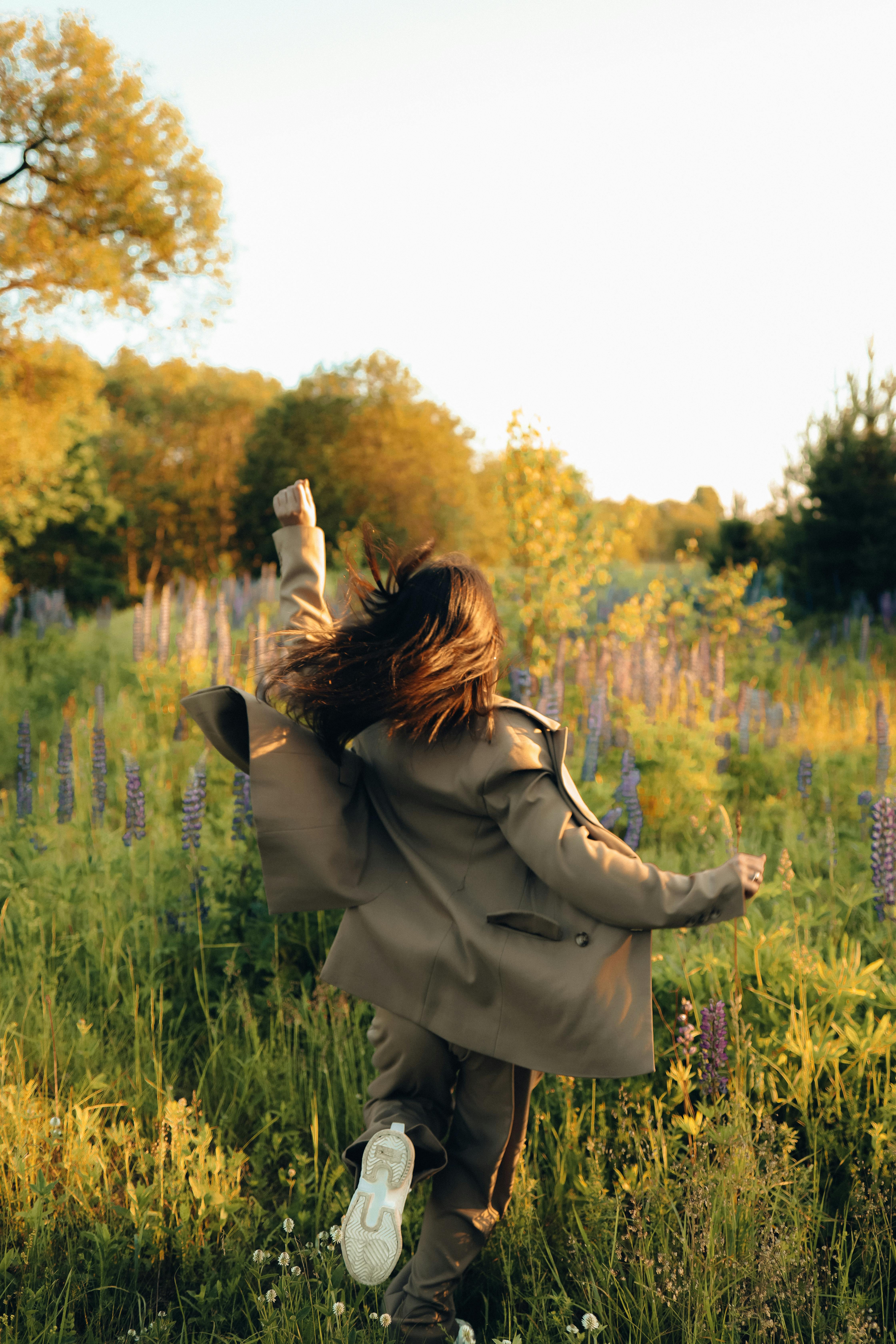 一名女子在阳光明媚的草地上无忧无虑地奔跑，拥抱自然和自由
