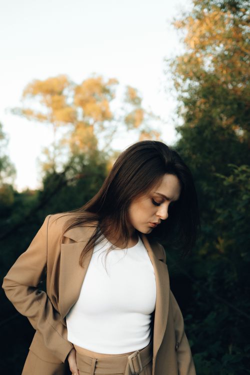 Free Elegantly dressed woman in a tan blazer set against a serene outdoor backdrop. Stock Photo