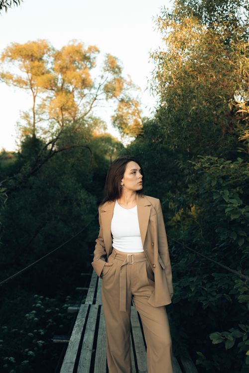 Free Portrait of a woman in a brown suit posing on a bridge in a lush forest setting, capturing natural elegance. Stock Photo