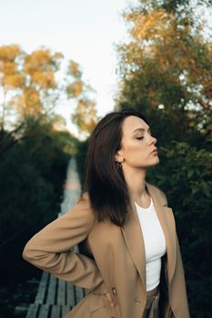 一位穿着棕色西装外套的女人，站在被大自然包围的木桥上