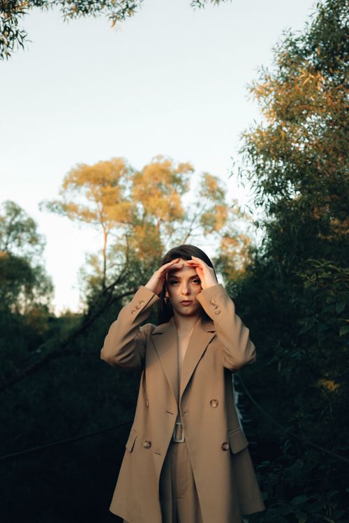 Free Young woman in a stylish brown suit poses gracefully in a lush, outdoor setting. Stock Photo
