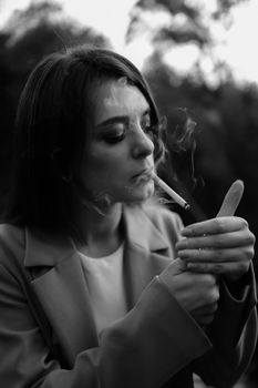 Black and white portrait of a woman lighting a cigarette outdoors.