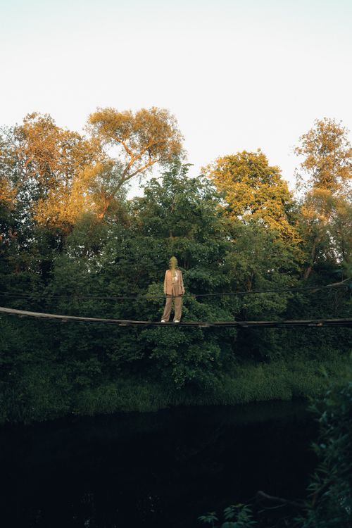Free A person walks a narrow footbridge above a river in a lush summer forest. Stock Photo
