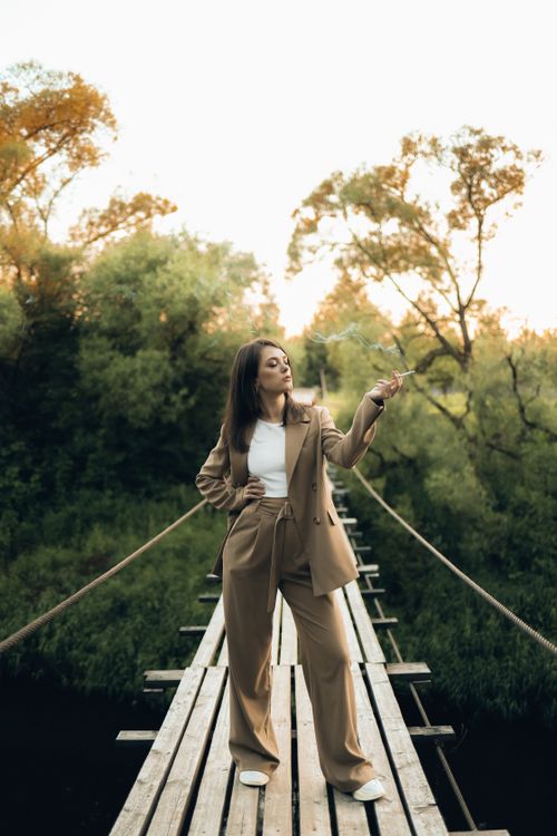 Free A fashionable woman in a brown blazer poses confidently on a rustic wooden bridge in nature. Stock Photo