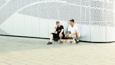 两名滑板爱好者坐在现代城市艺术墙旁休息