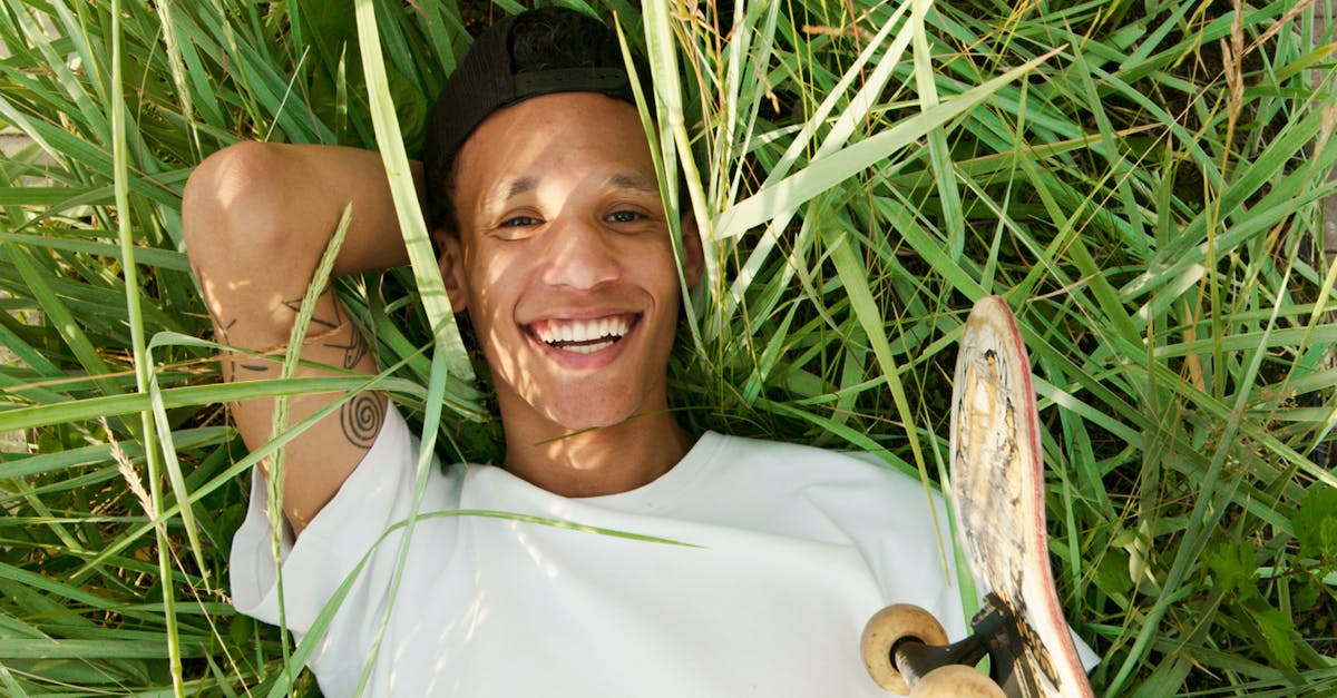 Smiling Woman in White Shirt Wearing Black Hat Lying on Green Grass