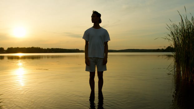 一名男子站在湖中，宁静的日落倒映在水面，四周环绕着大自然