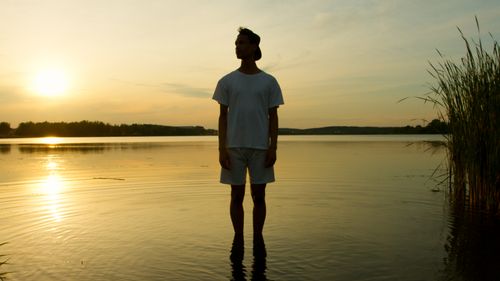 Free A man stands in a lake reflecting a serene sunset, surrounded by nature. Stock Photo