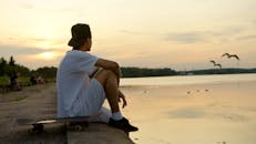 一个年轻人坐在湖边，拿着滑板，享受着宁静的日落