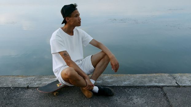 一名穿着白色服装的纹身滑冰运动员在宁静的湖边休息