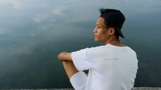 黄昏时分，一名身穿白衬衫、头戴白帽的男子凝视着平静的湖面及其倒影