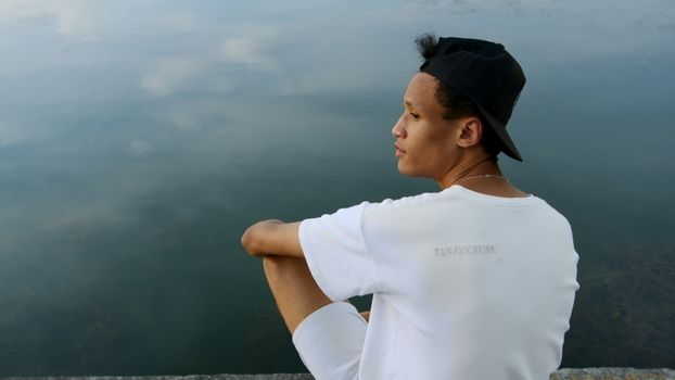 黄昏时分，一名身穿白衬衫、头戴白帽的男子凝视着平静的湖面及其倒影