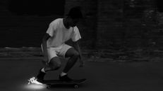 Man in White T-shirt and Shorts Sitting on Skateboard in Grayscale Photography
