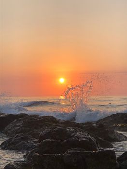 Fiery sunset over ocean waves crashing against rocks, capturing serene beauty.